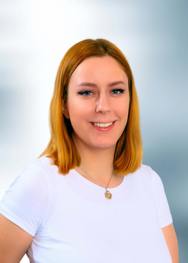 Laura Tomaszewski, Marketing, Hat rote schulterlange Haare und trägt ein weißes T-Shirt.