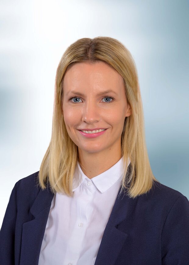 Laura Demir, Vertrieb Innendienst, hat blonde, schulterlange Haare und trägt eine weiße Bluse mit dunkelblauem Jacket.