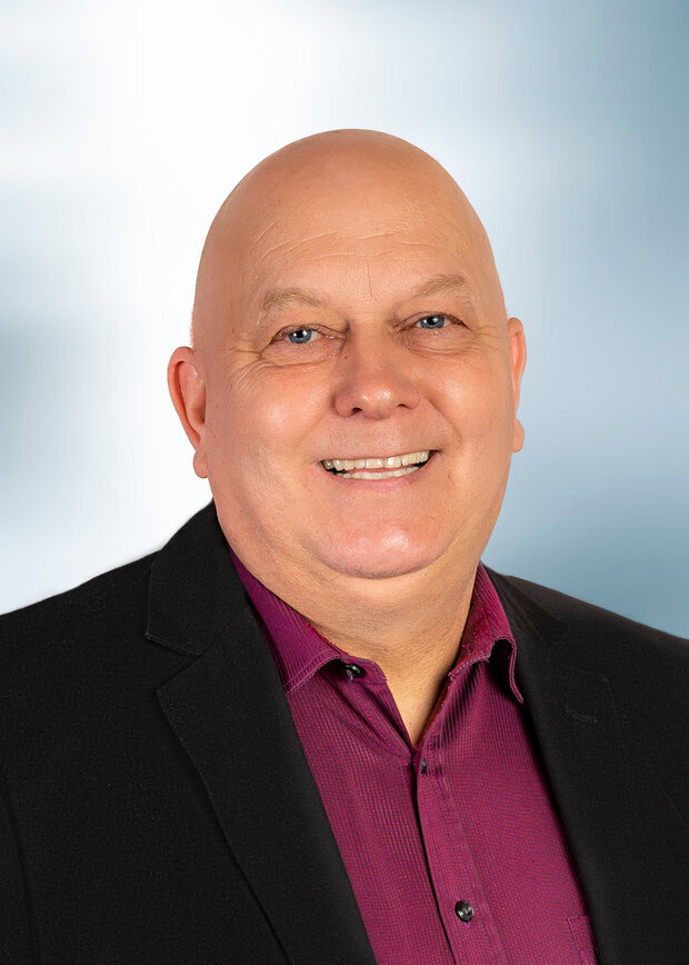 Uwe Vogt, Vertrieb Außendienst, hat eine Glatze und trägt ein dunkelrotes Hemd mit einem schwarzen Anzug.