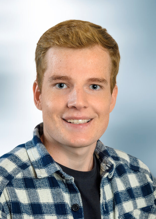 Sören Schröder, Verwaltung, hat kurze blonde Haare und trägt ein blau-weiß kariertes Hemd.