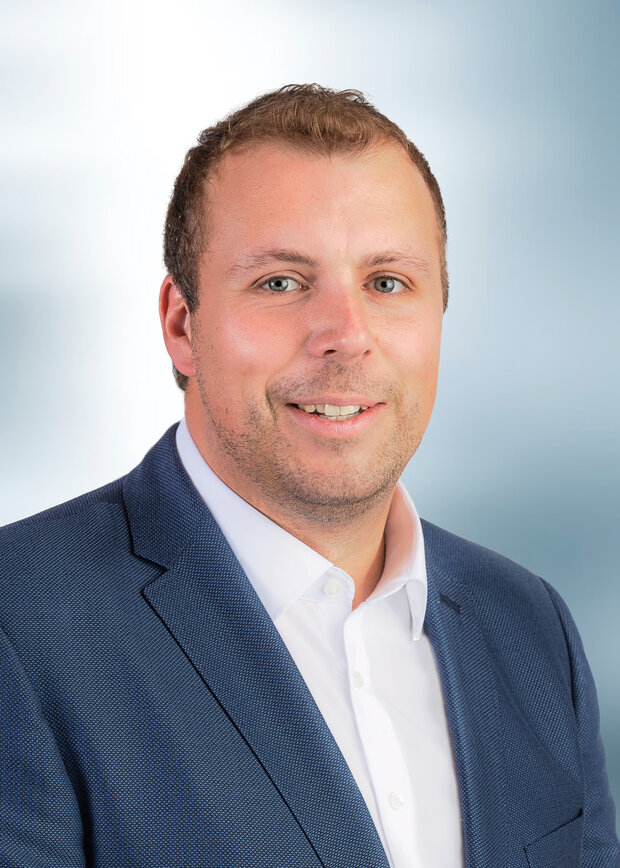 Benedikt Gadzinski, Instandhaltung, hat kurze dunkelblonde Haare und trägt ein weißes Hemd mit blauem Anzug.