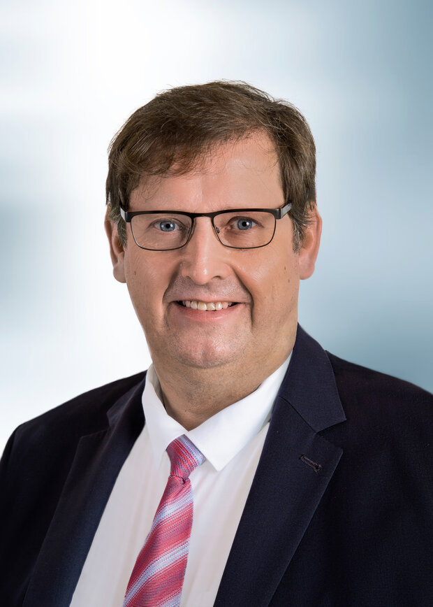 Stephan Langerbeck, Vertrieb Außendienst, hat braune Haare, trägt eine Brille und ein weißes Hemd mit dunkelblauem Anzug.