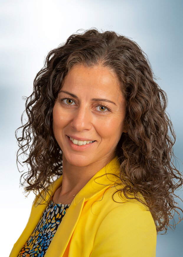 Necmiye Sariyar, Vertrieb Außendienst, hat dunkelbraune lockige Haare, trägt ein gelbes Jacket.