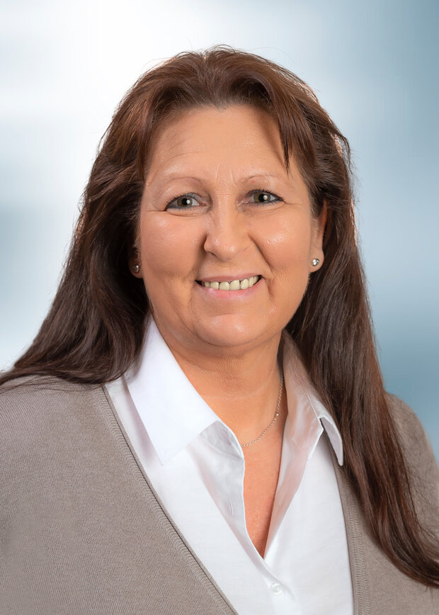 Christiane Wiegand, Verwaltung, hat lange braune Haare und trägt eine weiße Bluse mit einer beigen Strickjacke.