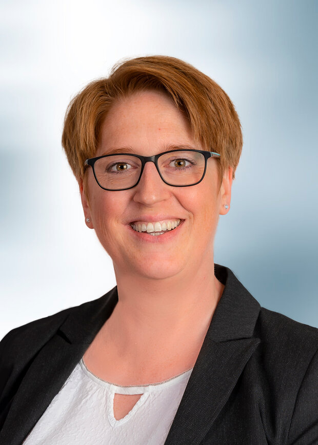 Carolin Leifeld, Verwaltung, hat kurze rote Haare, trägt eine Brille mit einer weißen Bluse und schwarzem Blazer.