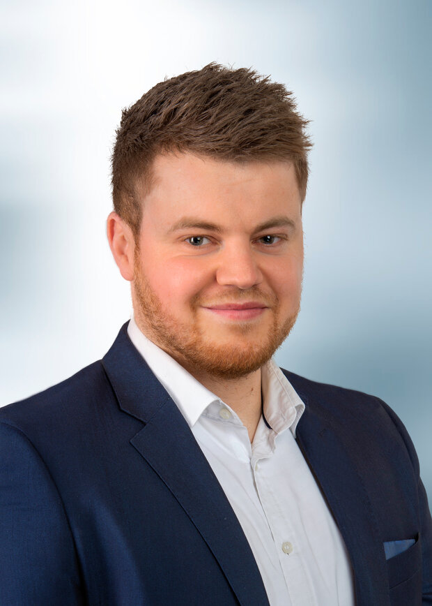 Dennis Ambrosius, Vetrieb, hat dunkelblonde Haare und trägt ein weißes T-Shirt mit dunkelblauen Anzug.
