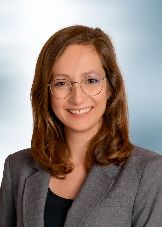 Linda Oppermann, Qualitätssicherung, hat braune schulterlange Haare, trägt eine Brille und ein schwarzer Shirt mit grauem Blazer.