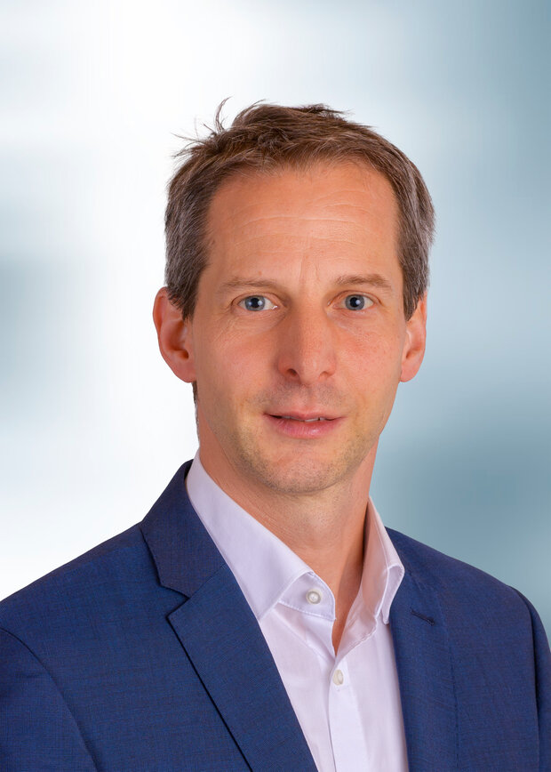 Thomas Schmidt, Produktion, hat dunkelblonde Haare und trägt ein weißes Hemd mit einem blauen Anzug.