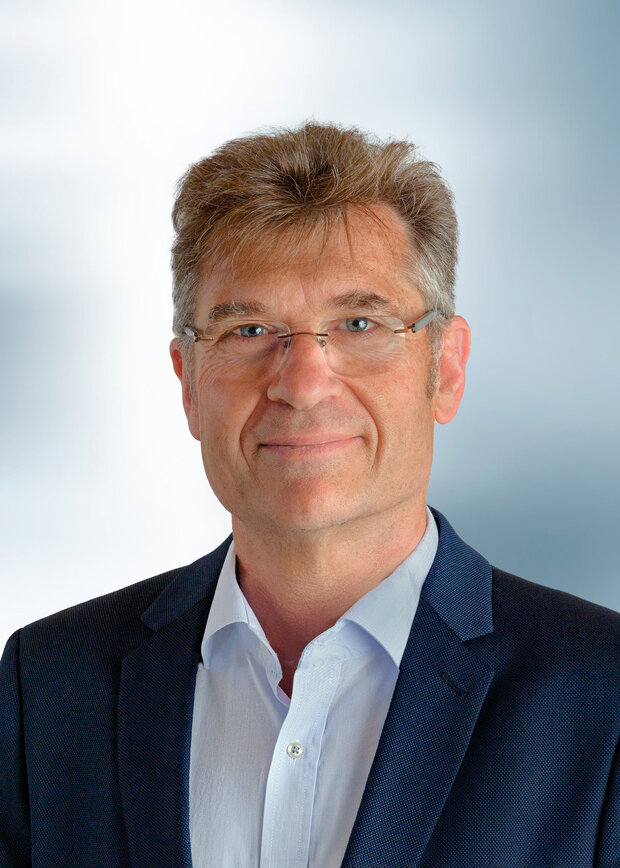 Manfred Schmidt, Geschäftsführung, hat kurze hellbraune Haare, trägt weißen Hemdkragen und dunkelblauen Anzug.