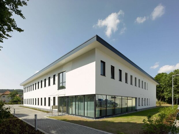 Weißes, zweistöckiges, modernes Gebäude mit einem Flachdach und einer großen Fensterfront.