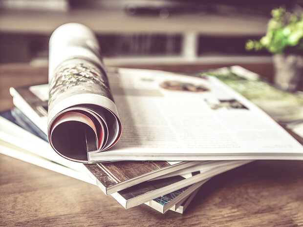 Ein Stapel Magazine, das Oberste liegt aufgeschlagen auf einem Tisch.