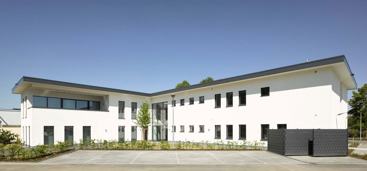 Weißes, zweistöckiges, modernes Gebäude in L Form mit einem Flachdach.