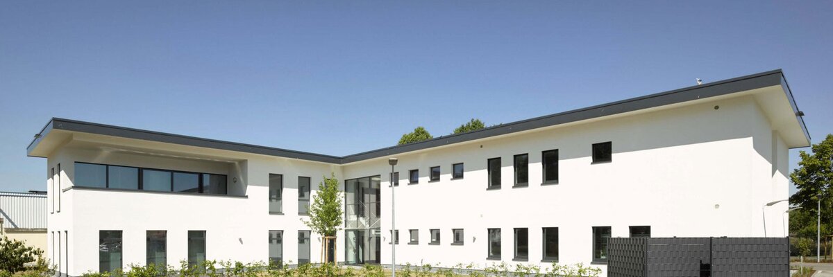 Weißes, zweistöckiges, modernes Gebäude in L Form mit einem Flachdach.