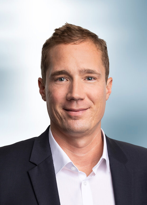 Hendrik Kuhn, Geschäftsführung, hat kurze dunkelblonde Haare und trägt ein weißes Hemd mit dunkelblauen Anzug.